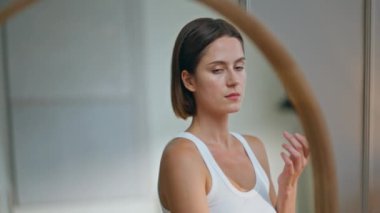 Yumuşak cilde nemlendirici krem süren bir kız. Evdeki kozmetik ürünleriyle yüzünü sulandıran güzel bir kadın. Cilt bakımı yapan genç bayan aynaya bakıyor..