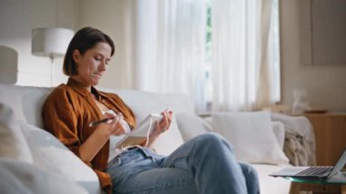 İnternetten ders izleyen bir kız rahat bir kanepede oturup kitap notları alıyor. Ciddi bir kız öğrenci uzaktan bilgisayar ekranına bakıyor. Akıllı kadın, not defterine bilgi yazıyor..