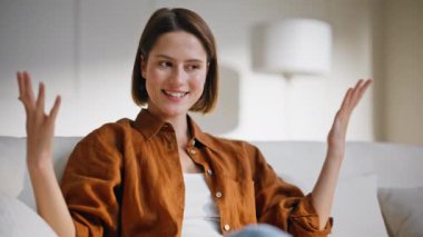 İnternetteki konferansta konuşan bir kız modern apartman kanepesinde oturuyor. Gülümseyen kadın videosu laptopu arıyor ve rahat koltukta haberleri tartışıyor. İçerideki sanal toplantıda konuşan neşeli uzaktan kumandalı danışman.