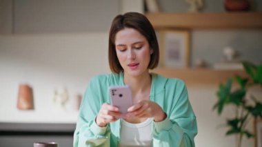 Modern bir apartman dairesinde cep telefonu mesajları yazan bir kadın. Evde akıllı telefon tutan gülümseyen genç bir kadın. Rahat kız cep telefonu uygulamasından online alımlar seçiyor.