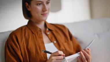 Rahat bir kız, rahat bir kanepede oturup günlük yazıyor. Gülümseyen genç bir kadın, içerideki deftere plan çizelgesini not alıyor. Mutlu yazar rahat koltuktaki not defterinde edebi eser yaratıyor.