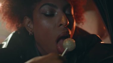 Gece lambalarının altında lolipop yalayan baştan çıkarıcı bir kız. Zeki Afro-Amerikan kadın şeker görünümlü kameranın tadını çıkarıyor. Otomobil kapısına dayanan kendinden emin, şehvetli bir kadın..