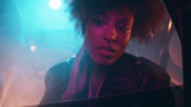 Renkli neon ışıkları altında araba camına bakan bir kadın. Kendine güvenen Afro-Amerikan bayan gecenin geç saatlerinde otomobilin arka koltuğunda oturuyor. Göz kamaştırıcı kız, gece hayatının tadını çıkarıyor..