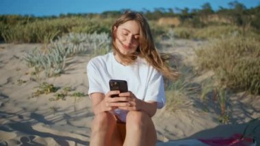 Rahat kız, Sandy Shore 'da cep telefonuna mesaj atıyor. Güneşli hafta sonlarında akıllı telefon kullanan çekici bir bayan plajda dinleniyor. Güzel rüzgarlı saçlı kadın sosyal medyayı kontrol ediyor. Trip yaşam tarzı konsepti 