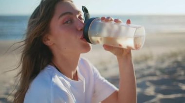 Yaz kadını okyanus portresindeki sahilden keyif alarak şişeden su içiyor. Rüzgarlı saçlı kadın, kumlu sahilde tek başına böğürtlenli içeceğini yudumluyor. Güzel kız açık havada taze ve sağlıklı bir içecek tadıyor. 