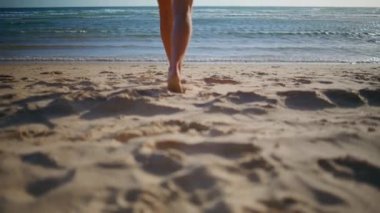 İnce bacaklar kumsalda yürüyor. Yaklaş. Okyanus kıyısına mayo giymiş romantik bir kız güneş ışığının arka görüntüsünün tadını çıkarıyor. Tanınmayan bir model, yaz tatilinde sahil şeridinde geziniyor. Tropikal adada dinlenen kadın