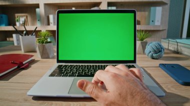 Profosyonel proje ev masasındaki yeşil ekran laptopunda yakınlaş. Bilinmeyen serbest çalışan elleri bilgisayar dokunmatik pedi kullanıyor. Ofisteki Chroma Key dijital aygıtında uzaktan yönetici çalışıyor.