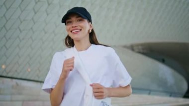 Neşeli koşu sokağında koşan bayan yaz sabahının keyfini çıkarıyor. Gülümseyen kadın kamerayla modern şehir binasının yakınında koşuyor. Siyah şapkalı. Mutlu sporcu kadın dışarıda sağlıklı fiziksel aktivitelerden hoşlanır..