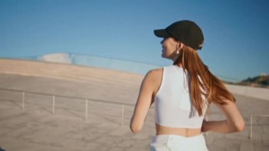Gülümseyen esmer, yaz caddesinde koşuyor ve dışarıda fiziksel aktivitelerden keyif alıyor. Mutlu kadın sporcu siyah şapkalı güneşli kasaba bölgesinde koşuyor. Enerjik sporcu kız güçlü sağlıklı vücudu eğitiyor..