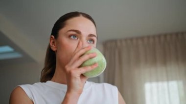 Hafif apartmanın iç tarafında yeşil smoothie içen bir kadın. Camdan vitamin içen rahat kadın sağlıklı yaşam tarzını destekliyor. Vücudun sağlığı için su içmeyi seven bir kız..