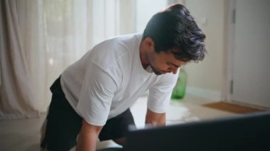 Profesyonel eğitmen çevrimiçi apartman katında diz çökmüş. Spor egzersizlerini açıklayan video dersi veren odaklanmış İspanyol adam. Motivasyonlu adam koçu sakin bir evde çalışıyor.
