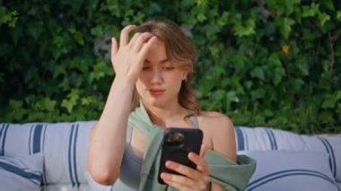 Güzel bir bayan rahat bir kanepede rahat bir şekilde cep telefonu bahçesinde oturuyor. Avluda cep telefonu tutarak saçlarını düzelten rahat bir kadın. Açık havada akıllı telefonda internette sörf yapan kaygısız bir kız.