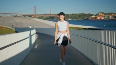 Sakin bir yaz sabahında şehir köprüsünde yürüyen sportif bir bayan. Aktif giyimli sakin esmer kendine güvenerek manzarayı keşfediyor. Rahatlamış sağlıklı bir kadın tek başına geziniyor ve dışarıda eğleniyor..