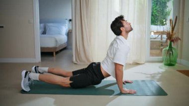 Yakışıklı sporcu, vücut esneme hareketleriyle yukarı doğru köpek yogası yapıyor. İspanyol sporcu hafif dairede esneklik eğitimi alıyor. Modern evde egzersiz yapan enerjik bir adam günlük egzersizin keyfini çıkarıyor..