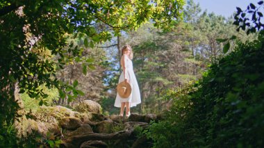 Romantik kız orman güneşi altında dikiliyor. Gülümseyen nazik kadın kamerayı doğanın tadını çıkarıyor. Yeşil ormanları tek başına düşünen dingin, güzel bir model. Basit zevkler konsepti 