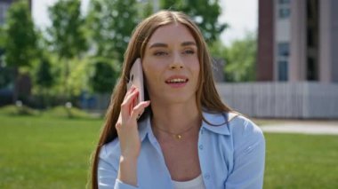 Green Park 'ın çimlerine yakın oturan neşeli bir kadın cep telefonuyla sohbet ediyor. Güler yüzlü kız güneşli bir günde dışarıda cep telefonu sohbetinden keyif alıyor. Rahatlamış esmer, çimenli çayırda akıllı telefondan arıyor..