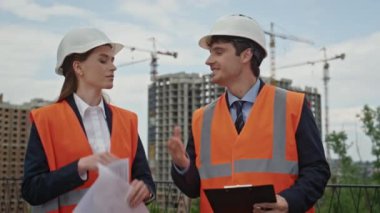 Mühendisler şehir şantiyesinde el sıkışma stratejisinde işbirliği yapıyorlar. Planlama projesinde gülümseyen profesyonel inşaatçılar planları gözden geçiriyorlar. Meslektaşlar inşaatı tartışıyor.