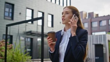 Enerjik iş kadını, cep telefonuyla iş yerini arıyor. Kahve fincanını da kapatmış. Modern binalardan geçen kendine güvenen profesyonel sohbet akıllı telefonlar. İçki içen kadın..