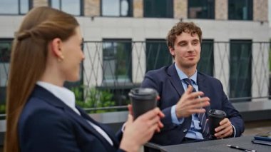 Kafeterya terasında kahve molasında rahatlamış iş kadını konuşuyor. Gülümseyen iş ortakları şirket stratejilerini açık hava toplantısında tartışıyor. Meslektaşlar fikirleri paylaşır.