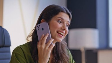 Şirketin iş yerinde cep telefonuyla konuşan neşeli bir bayan. Akıllı telefon görüşmesiyle haberleri tartışan gülümseyen kadın uzaktan çalışıyor. Mutlu iş kadını ev ofisinde dostça sohbetin keyfini çıkar..