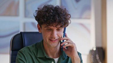 İş adamı modern ofis alanlarında oturarak dostça konuşmanın tadını çıkarıyor. İş yerinde çalışan kıvırcık saçlı menajerin akıllı telefon konuşması portresi. Gülümseyen girişimciler sıradan telefon konuşmaları yaparlar..