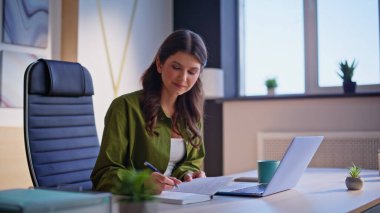 Şirket çalışanı, modern işyerindeki defter defterine fikirleri not ederek proje yaratıyor. Başarılı iş planı üzerine düşünen gülümseyen bir iş kadını. Ofiste dizüstü bilgisayarda çalışan profesyonel biri..