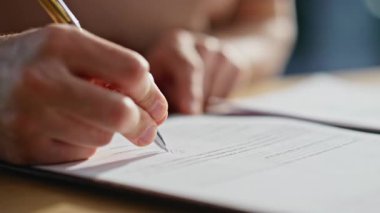 Ofis masasında yakın çekim el imzalama sözleşmesi. Organize çalışma alanındaki yasal belgeleri onaylayan tanınmamış bir işadamı. Erkek parmaklar kalem tutuyor. Pazarlıktan sonra resmi anlaşmaya imza atıyorlar..