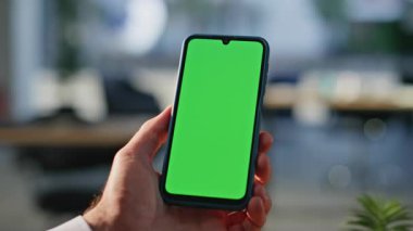 Elinde yeşil ekran cep telefonu olan bir adam ofiste video görüşmesi yapıyor. Bilinmeyen iş adamı Chroma Key cep telefonunda çevrimiçi uygulama tarıyor. Freelancer içeriden akıllı telefon mesajı okuyor.