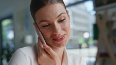 İş yerinde cep telefonuyla konuşan, evraklara bakan yakın bir kadın. Gülümseyen iş kadınının portresi. Omzuyla akıllı telefonu tutuyor. Ofiste cep telefonu konuşmalarında belgeleri tartışan genç bayan.