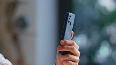 Ofiste cep telefonunu tutan iş adamı elleri yakın plan. Gülümseyen adam yöneticisi iş yerinde akıllı telefon ekranı tarama uygulamasını dinliyor. Kapalı alanda cep telefonu mesajı okuyan pozitif erkek serbest yazar.