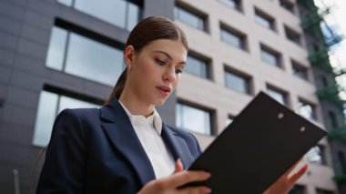 Odaklanmış iş kadını şehir merkezinde evrak işleriyle uğraşıyor. Modern şehir sokaklarında belgeleri inceleyen profesyonel kadın portresi. Gülümseyen bayan girişimci ofis dışındaki iş raporundan memnun..
