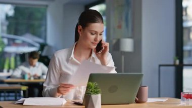 Yönetici arıyor. Dizüstü bilgisayar arıyor. Ofis açık alanda yakın plan çekimde. İş yerinde akıllı telefondan konuşan neşeli bir iş kadını. Zarif kadın CEO cep telefonu konuşmasında rapor sunuyor.
