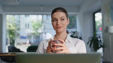 Ofis çalışanı elinde kahve fincanı tutarken yakın plan çekimde oturuyor. Rahat iş kadını içecek görünümlü dizüstü bilgisayar ekranı içiyor. Çekici genç bayan yönetici modern işyerinde iş molası veriyor..