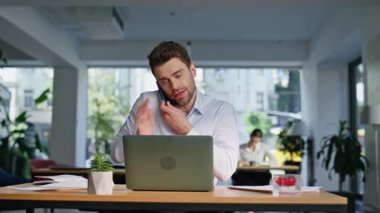 İş danışmanı, modern çalışma alanındaki çalışma masasında akıllı telefondan konuşuyor. Gülümseyen yönetici ofisteki dizüstü bilgisayarını arıyor. Çalışan telefon görüşmelerinde kağıtlara bakıyor..