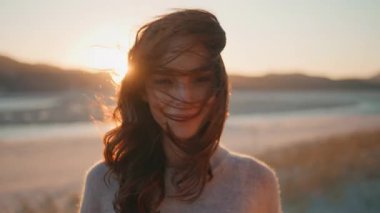 Rüzgarlı günbatımında portre kadın doğa kamerası. Altın gece ufkunda poz veren güzel esmer, saçları rüzgarlı yakın plan. Mutlu kadın, dingin yaz alacakaranlığının tadını çıkarıyor..