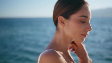 Deniz kıyısında beyaz şık mayo giymiş esmer bir portre. Okyanus dalgalarında poz veren kaygısız kadın turist yumuşak bir gülümsemeyle kameraya bakıyor. Güzel yaz deniz manzarasında duran mutlu bayan..