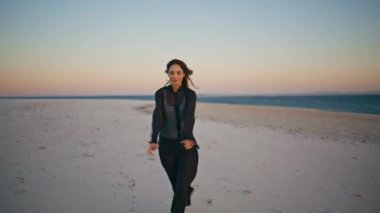 Rüzgarlı deniz kıyısından hoşlanan bir kadın yalnız başına dinleniyor. Gülümseyen model esmer kumsalda yürüyen pembe günbatımı ufkunda. Mutlu bayan gezgin, güzel okyanus kıyısında bir akşam geçiriyor. Deniz yolculuğu kavramı.