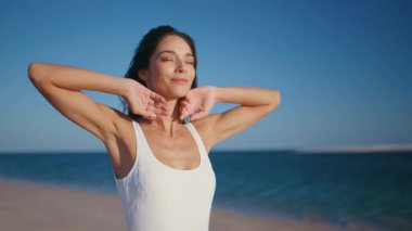 Deniz doğasından hoşlanan bir kadın sahilde yakın planda gökyüzünü temizlemek için el kaldırıyor. Altın kumlu sahil şeridinde yürüyen mutlu tatilciler. Kaygısız esmer, beyaz mayo giymiş güneşli sahilde geziniyor..