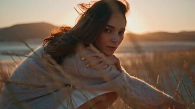 Kuru çim tarlasında poz veren kız yaz günbatımının tadını çıkarıyor. Altın ufukta mutlu ve çekici bir kadın var. Rüzgarlı doğada çömelmiş muhteşem bir model. Uzun saçlı bayan yalnız başına dinleniyor.