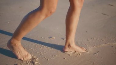 Kumsalda çizim yapan kadın bacakları. Bronzlaşmış kadın ayakları okyanus kıyısında ayak izleri bırakıyor. Gülümseyen güzel esmer güneşli deniz kıyısının tadını çıkarıyor. Gülümseyen kız turist yaz mevsiminde yürüyor