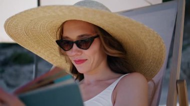 Portre kızı sahilde kitap okuyor ve yaz tatilinin tadını çıkarıyor. Hasır şapka takan güzel bir kadın deniz kıyısında güneşlenen bir kitap tutuyor. Kaygısız tatilci kıyıda edebiyat hobisine daldı..
