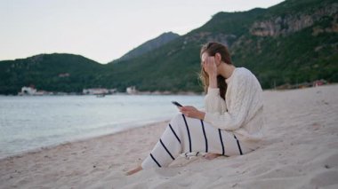 Sahilde akıllı telefonlara bakıp sakin alacakaranlığın tadını çıkaran bir kız. Huzurlu, güzel bir kadın cep telefonu mesajı okuyor. Yumuşak sahil kumunda oturuyor. Tasasız gezgin tatil anılarını paylaşarak içerik yaratıyor.