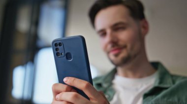 Ofiste akıllı telefonu tutan erkek elleri kapalı. Genç gülen işadamı iş yerinde cep telefonunu olumlu ruh halinde kullanıyor. Neşeli adam cep telefonunu arıyor. Sosyal medyada geziniyor. 