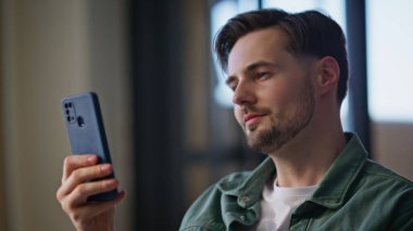 Apartman dairesinde komik videolar izleyen gülen adam. Mutlu gülen adam haberlere bakıyor ve cep telefonuyla eğleniyor. Neşeli erkek sosyal ağların cep telefonunu izliyor 