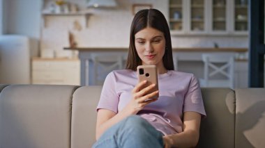 Evdeki koltukta cep telefonu kullanan mutlu bir bayan. Pozitif kadın hafta sonu evde akıllı telefondan alışveriş yapıyor. Genç ve çekici bir kız cep telefonu uygulamasında internetten alışveriş yapmayı düşünüyor.