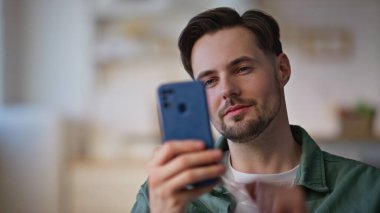 Evdeki adam sabahları cep telefonu kullanıyor. Neşeli adam gülücükle mesaj okuyor apartmanın içinde oturup komik videolar izliyor. Mutlu esmer yazıcı cep telefonu ekranı sosyal medyada geziniyor