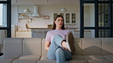 Yorgun bir kadın kanepede rahat bir şekilde oturur ve stres hisseder. Violet tişörtlü yorgun bir kadın sorunlarla dolu bir evde rahat bir kanepeye düşüyor. Stresli kız baş ağrısı çeken kafaya dokunuyor. 