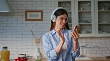 Yemek pişirirken akıllı telefon kullanan bir bayan. Kulaklıklı neşeli bir kadın cep telefonunda şarkı söylerken müzik dinliyor. Kulaklıklı gülümseyen kız cep telefonuyla aşçılığın tadını çıkarıyor.