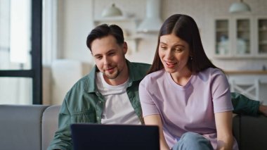 Dizüstü bilgisayardan romantik çift videosu. Oturma odasındaki kanepeye yakın çekim. Güzel bir kadın, internette duygusal olarak el sallıyor. Rahat eşler bilgisayarla yapılan uzak konferansın keyfini çıkarın