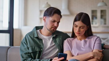 Evde yakın çekim yapan bir çift kanepe. Endişeli adam akıllı telefonuyla esmer kız arkadaşına ekranı gösteriyor. Hayal kırıklığına uğramış üzgün çift evde kötü haber veriyor. Duygusal eşler birlikte konuşur.